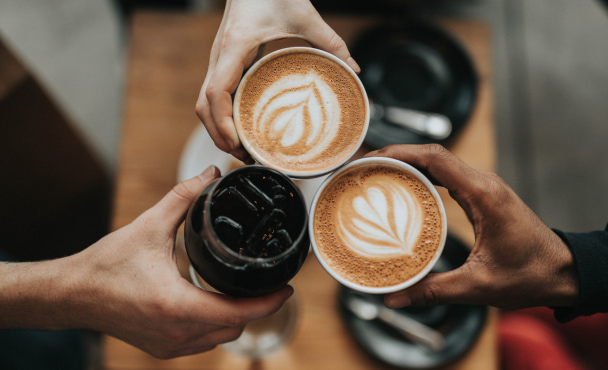 Three friends clinking coffee cups at a South Yarra café, including lattes with latte art and an iced coffee