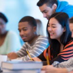 International students are working on a group assignment in an Australian university classroom. They are using a computer to do research online.