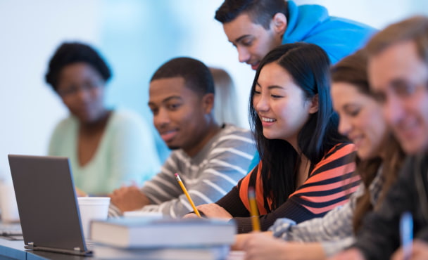 International students are working on a group assignment in an Australian university classroom. They are using a computer to do research online.