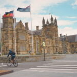 A person riding a bike in front of a building at the University of Sydney
