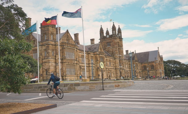 A person riding a bike in front of a building at the University of Sydney