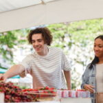 Multiethnic friends shop for fresh produce at an outdoor market. They look happy and relaxed while selecting fruit and vegetables.