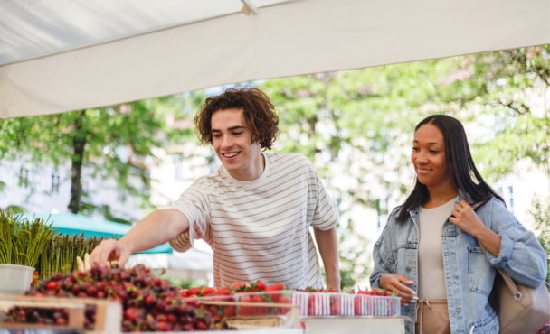 Multiethnic friends shop for fresh produce at an outdoor market. They look happy and relaxed while selecting fruit and vegetables.