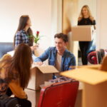 A group of four university students move into their shared flat , and start to unpack boxes. One male student is looking through his boxes in the foreground