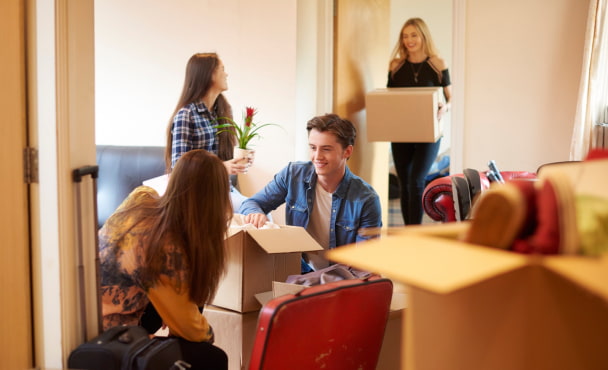 A group of four university students move into their shared flat , and start to unpack boxes. One male student is looking through his boxes in the foreground