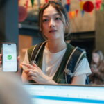 Young woman showing her online booking and check-in details on her smartphone to the receptionist after confirming her reservation.