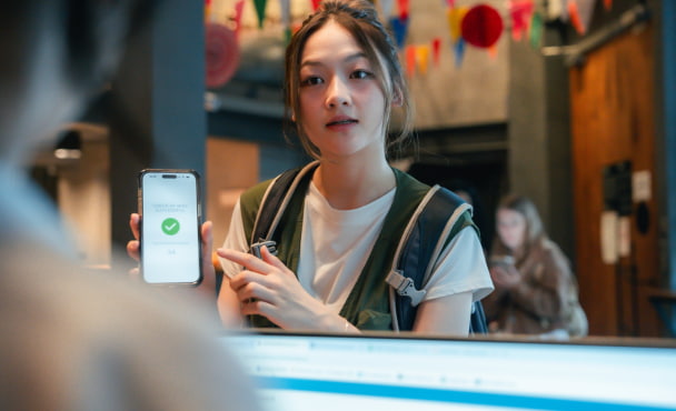 Young woman showing her online booking and check-in details on her smartphone to the receptionist after confirming her reservation.
