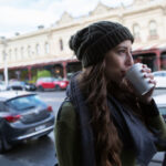 Waist up view of a young woman enjoying coffee as she walks through South Melbourne