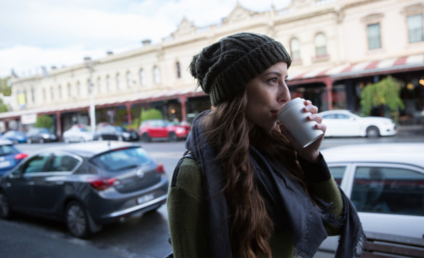 Waist up view of a young woman enjoying coffee as she walks through South Melbourne