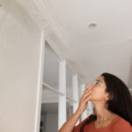 Shocked student inspecting apartment with wall damage. Student looking at ceiling and wall, feeling frustrated, upset.