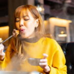 Young Asian woman eating traditional food spicy Mala hotpot dish with chopsticks in Chinese restaurant.