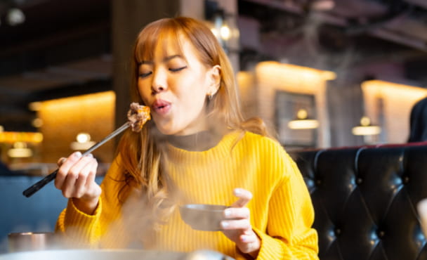Young Asian woman eating traditional food spicy Mala hotpot dish with chopsticks in Chinese restaurant.
