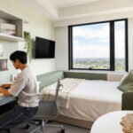 Male student studying on laptop on study desk of studio apartment at Iglu Waterloo Student Accommodation