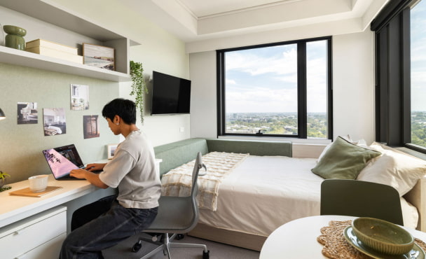 Male student studying on laptop on study desk of studio apartment at Iglu Waterloo Student Accommodation