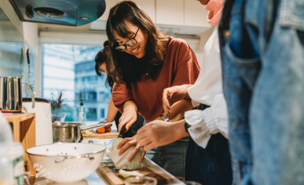 Group of friends preparing dinner in a shared student apartment together in the kitchen