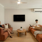 Modern student accommodation living room with two students on red lounges with a coffee table in between and a television on the wall.