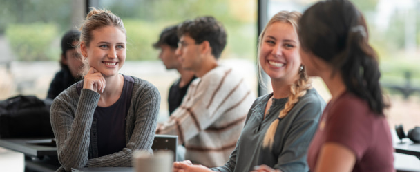 Three young adults collaborate and converse in a bright classroom, fostering teamwork and connection. The modern, cheerful atmosphere enhances learning and creativity, emphasizing a sociable and inclusive environment for education.