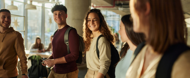 Group of happy students communicating while walking through a school hallway.