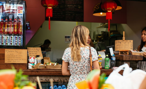 Woman in floral dress ordering at a snack bar with Asian decor and light refreshments visible.