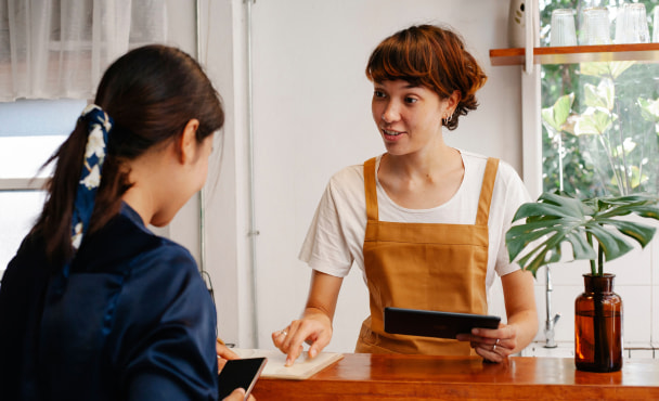 A barista helping a customer with a tablet in a modern café setting. Natural interaction.
